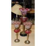 A cranberry glass and gilt metal paraffin lamp, 74cm high overall and a pair of smaller paraffin