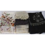 A black embroidered wool shawl; together with a black silk stole; a cream embroidered shawl; and