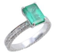 An emerald and diamond ring, the step cut emerald claw set above a diamond...  An emerald and