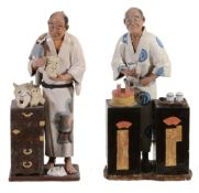 A Pair of Japanese Pottery Figures, one of a tea seller standing behind his...  A Pair of Japanese
