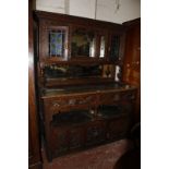 A late Victorian oak dresser with a mirrored back flanked by stain glass cabinets, richly carved