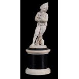 A Dieppe ivory figure of a peasant boy,   late 19th century,  standing with folded arms and tree