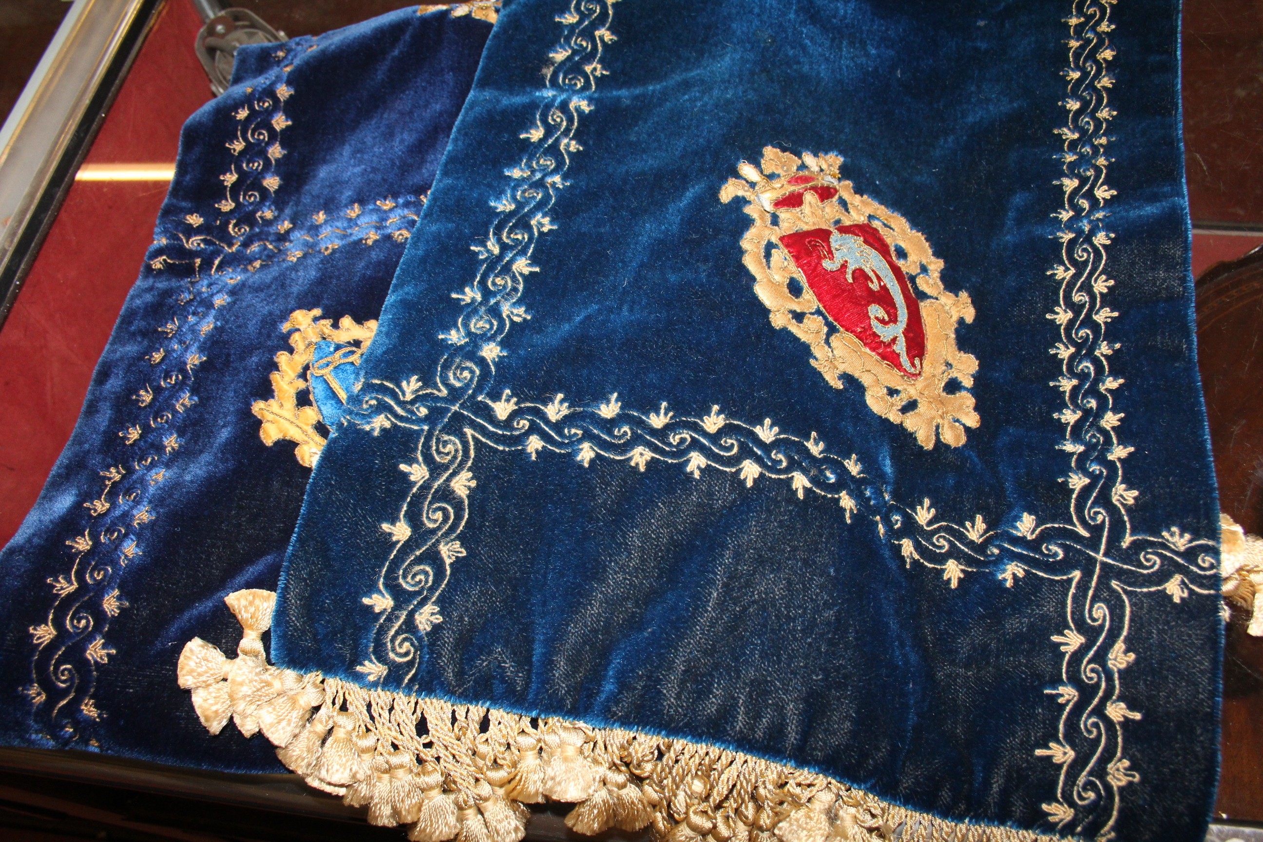 Two blue velvet and embroidered wall hangings, with appliqué crests and gilt foliate scroll