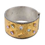 A gem set cuff bangle, the two colour broad hinged bangle set with various...  A gem set cuff