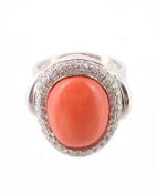 A diamond and coral cluster dress ring, the oval cabochon coral panel within a surround of