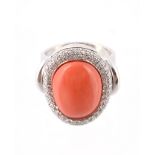 A diamond and coral cluster dress ring, the oval cabochon coral panel within a surround of