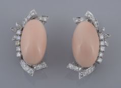 A pair of diamond and coral ear clips, the oval cabochon coral panels within an abstract diamond