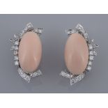 A pair of diamond and coral ear clips, the oval cabochon coral panels within an abstract diamond