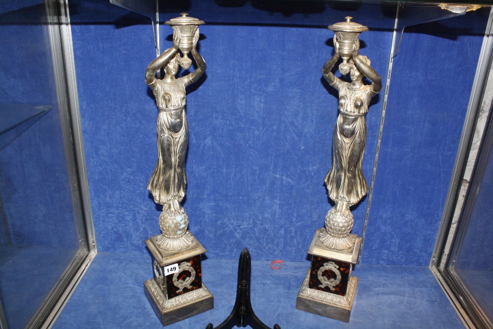 A pair of Empire style silver coloured metal figures and faux tortoiseshell clad base, 63cm high