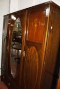 An Edwardian mahogany wardrobe with floral inlay having a central oval mirrored door.140cm x 184cm.
