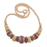 A ruby bead necklace, the central polished ruby bead in a pierced scallop setting between further
