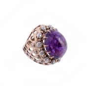 An amethyst and diamond ring, the central oval cabochon amethyst in a claw setting within a