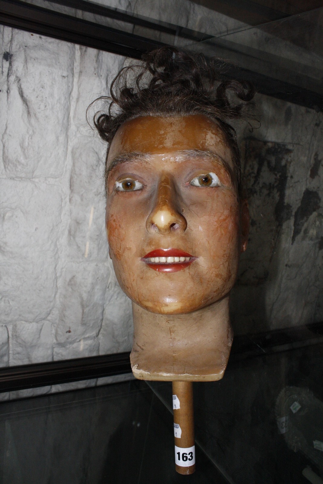 A wax mannequin head of a man with real hair wig, glass eyes, wooden handle 32.5cm (not including