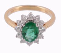 An emerald and diamond cluster ring, the central oval shaped emerald in a...  An emerald and diamond