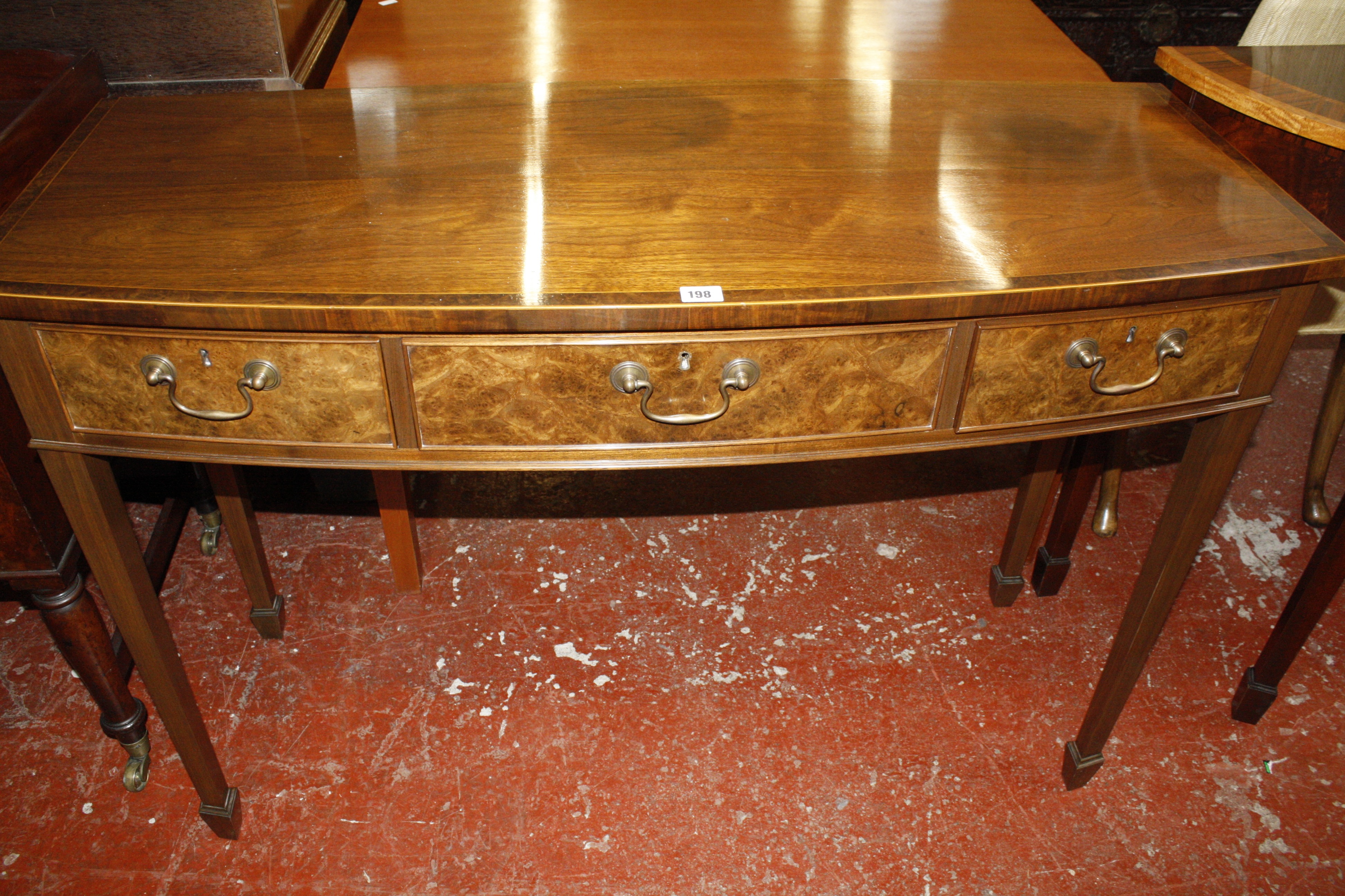 A bow front mahogany side table with three walnut faced drawers. 121cm wide.