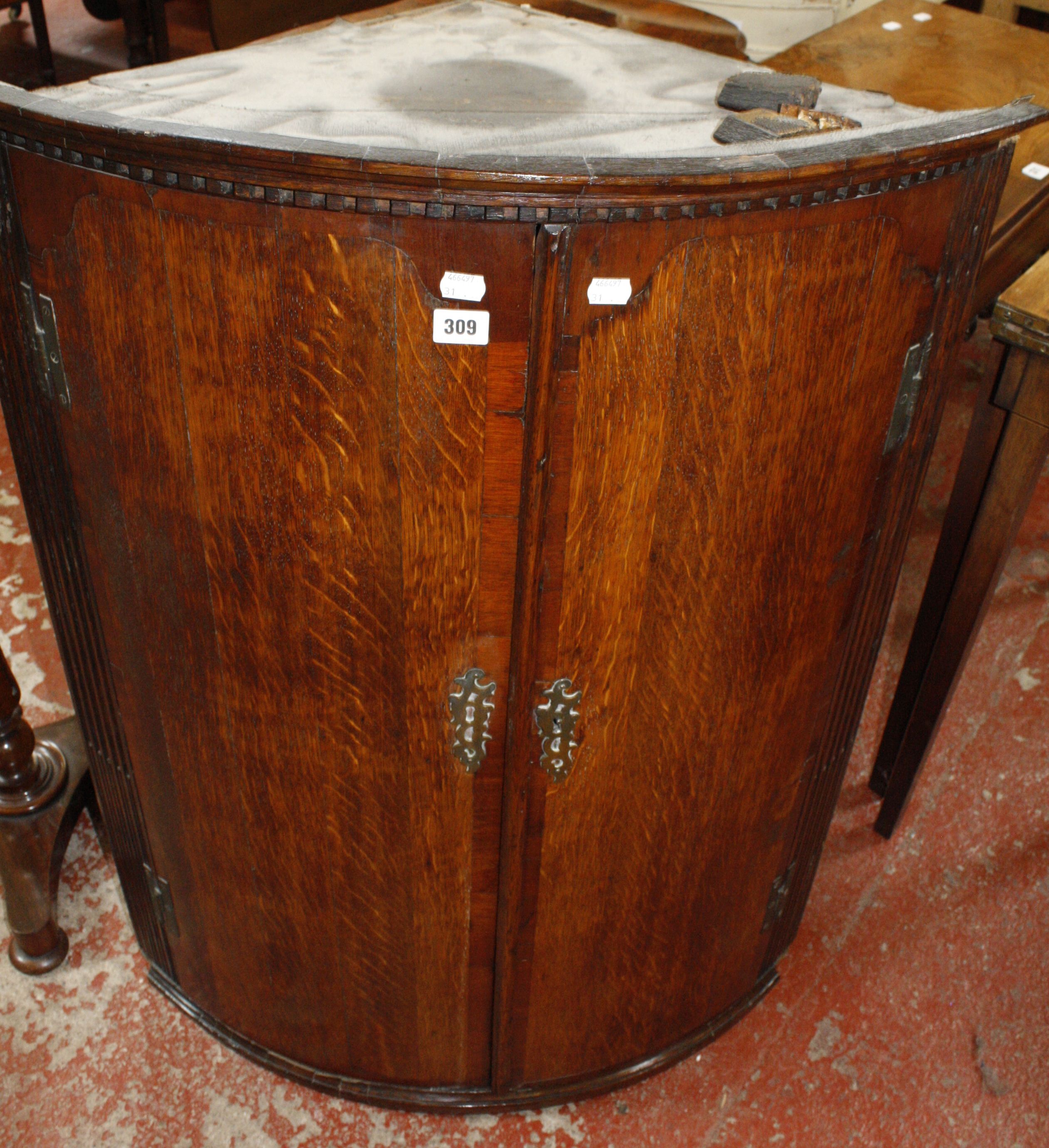 A George III oak bow front hanging corner cupboard with a dentil cornice, the panel doors having