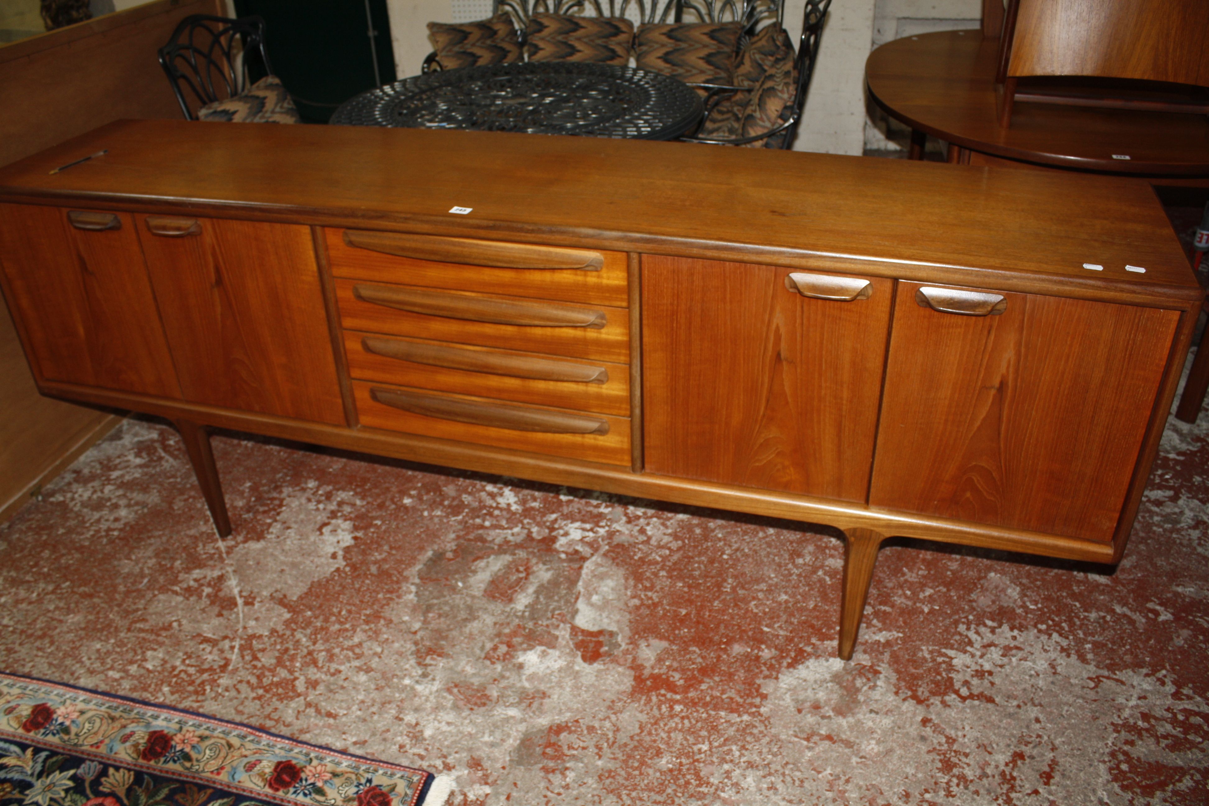 A teak sideboard with four central drawers flanked by cupboards on tapering legs bearing label '