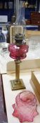 A Victorian oil lamp with cranberry glass shade and reservoir, on a brass reeded column base, 74cm