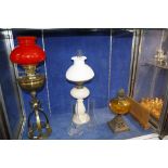 A Victorian white opaline oil lamp, a Victorian brass lamp with bright red glass shade and a cast