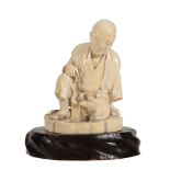 A Japanese Tokyo School Ivory Okimono depicting a waraji maker seated and... A Japanese Tokyo School