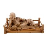 An Ivory Okimono of a Reclining Man , dressed in a diaper patterned loose... An Ivory Okimono of a