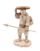 An Ivory Okimono of a Fisherman, he stands on an irregular base strewn with... An Ivory Okimono of a