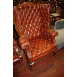 A Georgian style red leather wing armchair with button back and carved legs