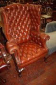 A Georgian style red leather wing armchair with button back and carved legs