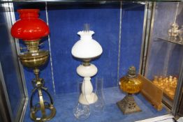 A Victorian white opaline oil lamp, a Victorian brass lamp with bright red glass shade and a cast
