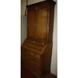 An early 19th Century oak bureau bookcase with a dentil cornice, the panelled cupboard doors