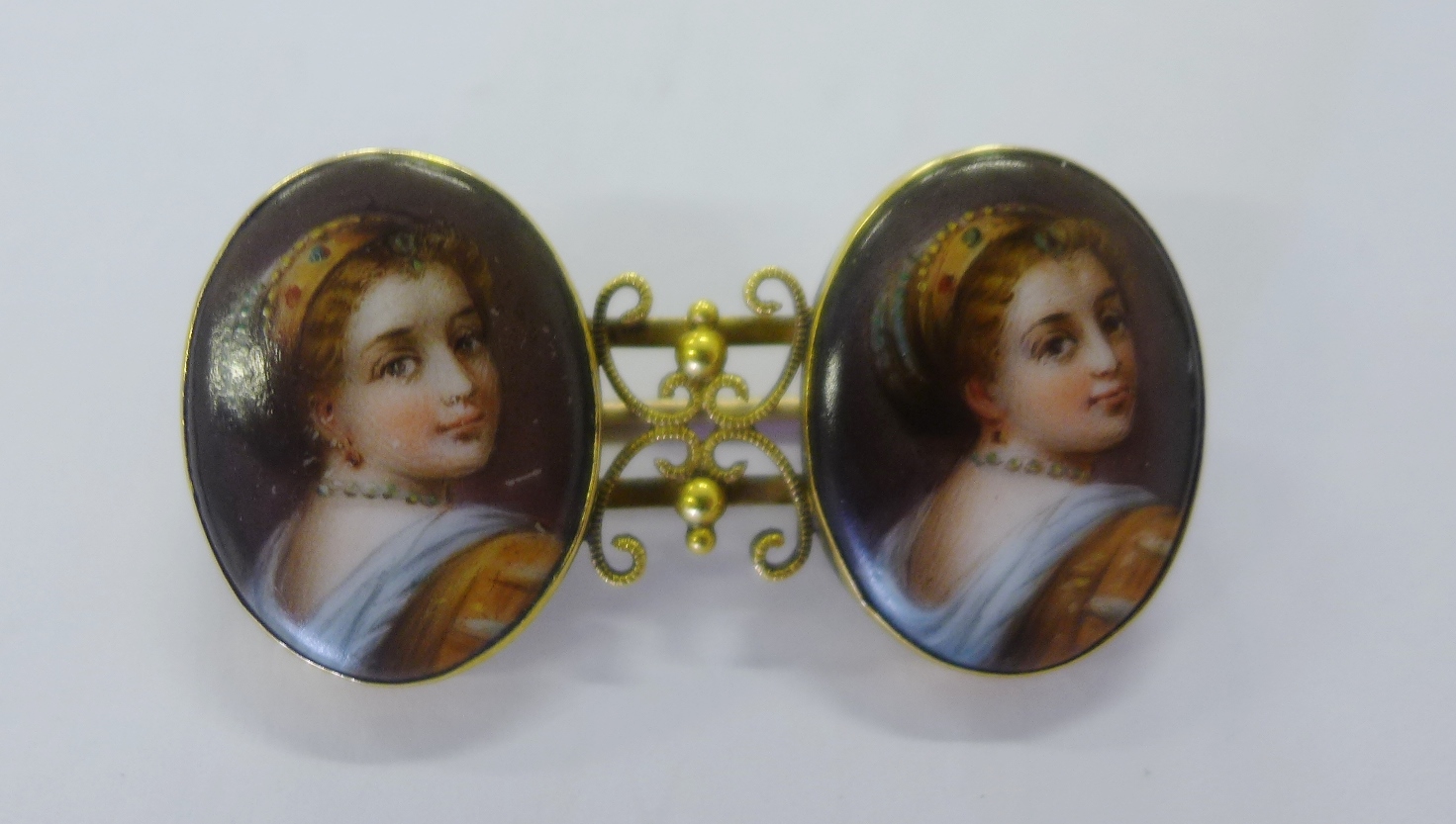 A 15ct gold bar brooch mounted with two oval porcelain plaques painted with a female looking over