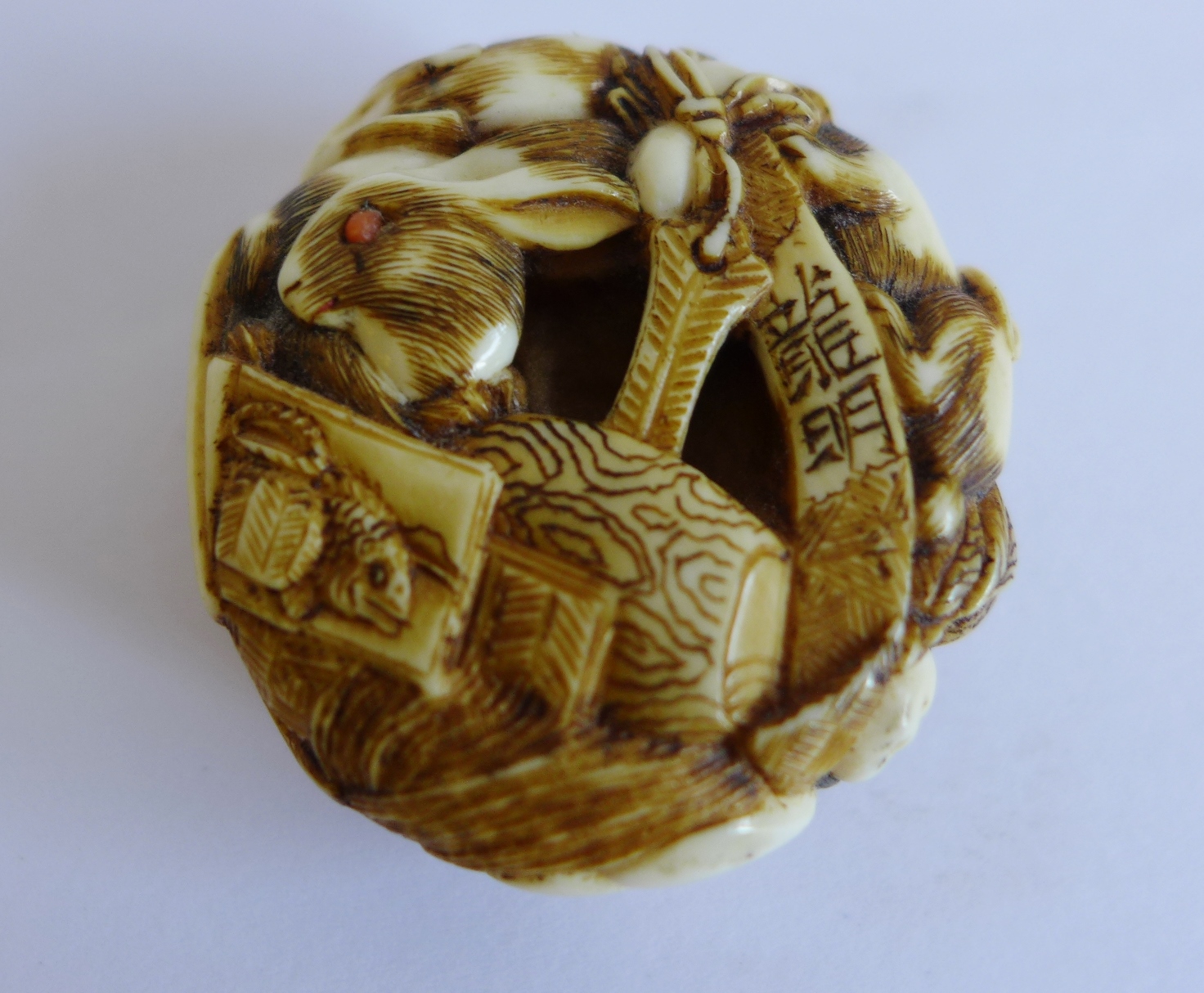 A Japanese ivory netsuke, the small circular pebble intricately carved with many hares having