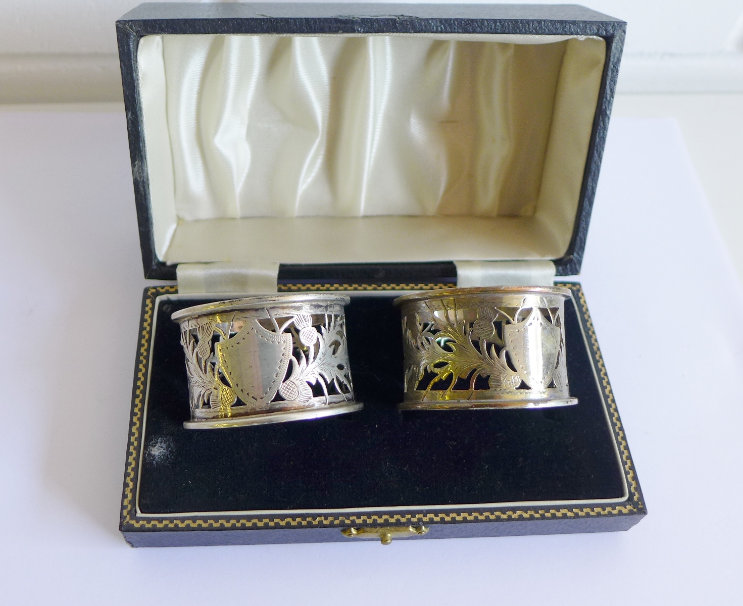 A pair of Chester silver pierced napkin rings, with thistle pattern and vacant shield cartouche,