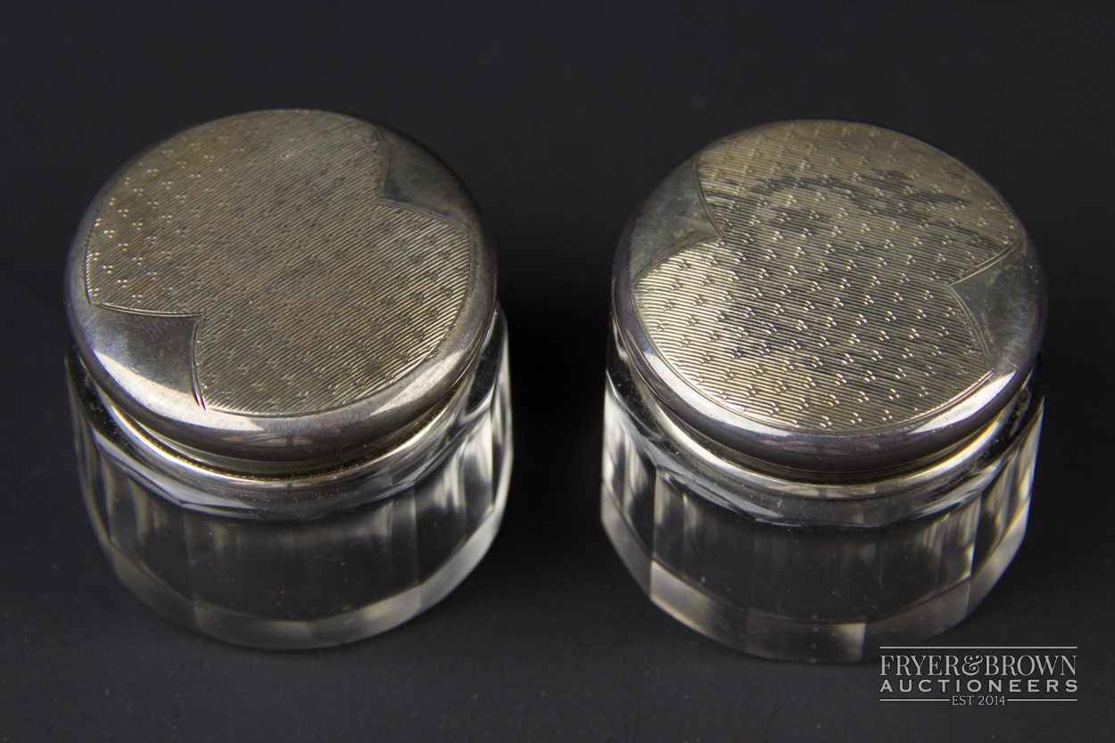 A pair of cut glass rouge pots, the silver lids with gilt interiors and engine turned decoration top