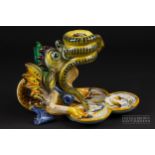 A Cantagalli maiolica grotesque candlestick, formed as a winged beast holding a coiled snake in