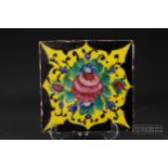 A Qajar tile, brightly glazed with a Damascus rose, two buds and blue flowers on a yellow reserve,