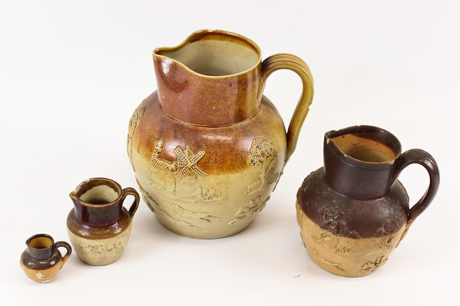 A group of four stoneware jugs, sprigged with topers and hunting scenes, including a miniature