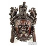 A Chinese carved hardwood wall mask of a warrior with fierce expression, wearing an elaborate