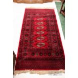 A wool rug, the dark red ground with six central medallions with subsidiary borders, 178 x 90cm