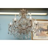 A brass framed chandelier with six candle effect lights, crystal drops and swags between arms