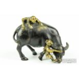 A Chinese bronze of a bull being restrained by two figures, one on its back, the other holding its