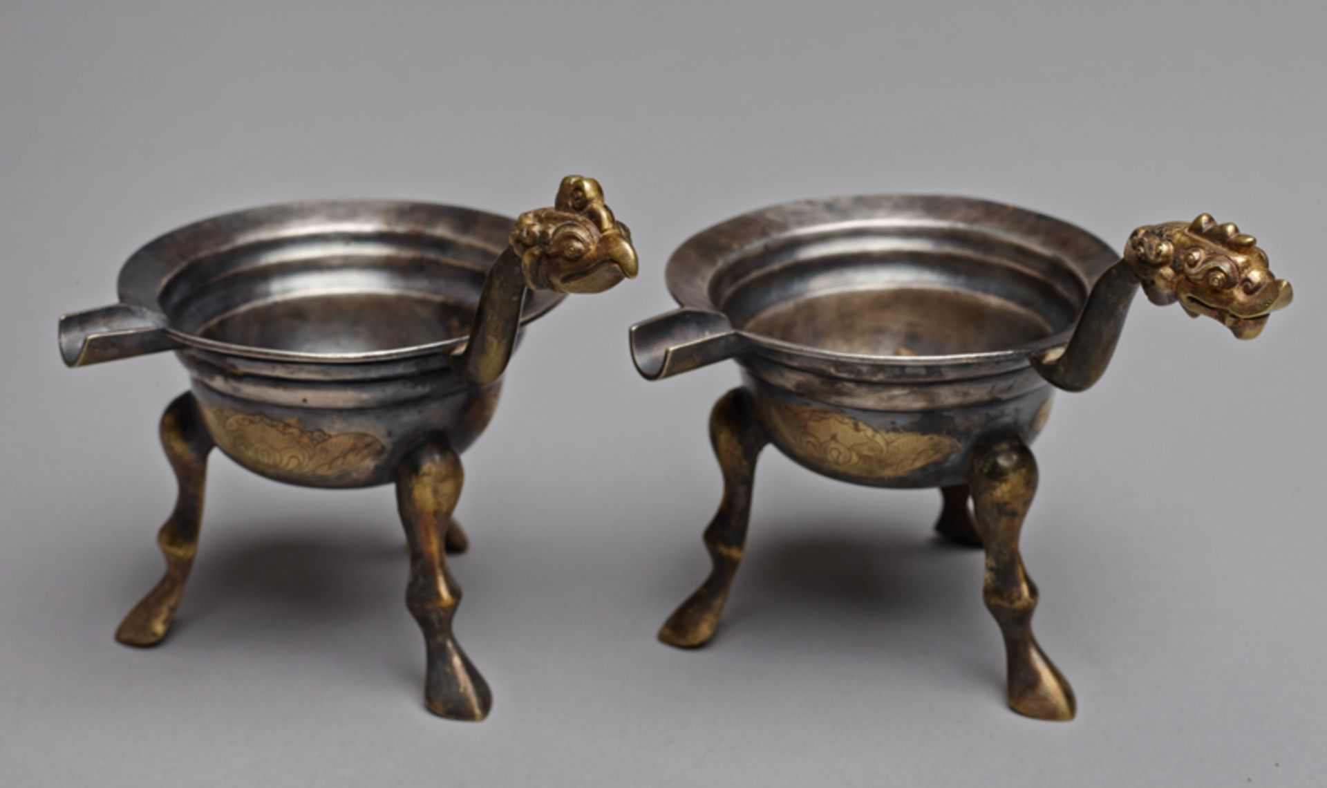 TWO TRIPOD VESSELS WITH HANDLE AND SPOUT  Silver and gilding. China, presumably Six Dynasties period