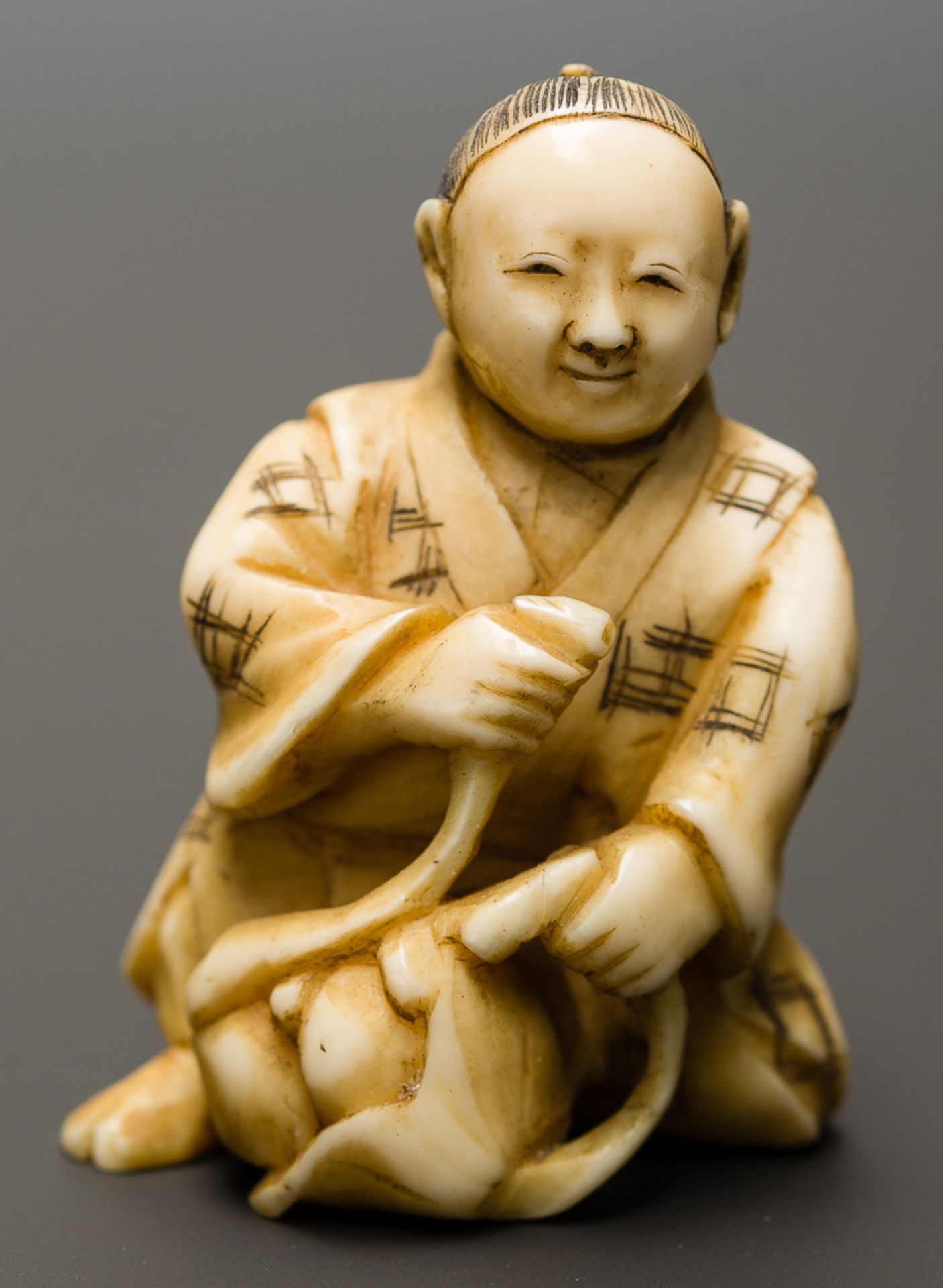 MANN MIT FRÜCHTEN
Netsuke-Okimono, Elfenbein. Japan, Meiji-ZeitHalb knieender Mann, der aus seinem