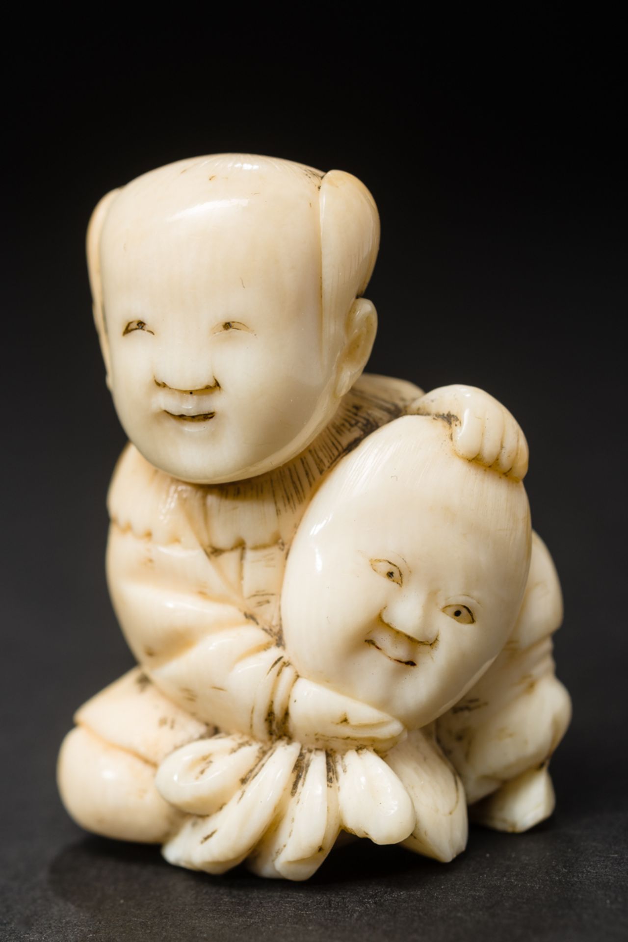 KARAKO-KNABE MIT MASKE
Netsuke, Elfenbein. Japan, 19. Jh.Am Boden sitzender Karako, ein chinesisch