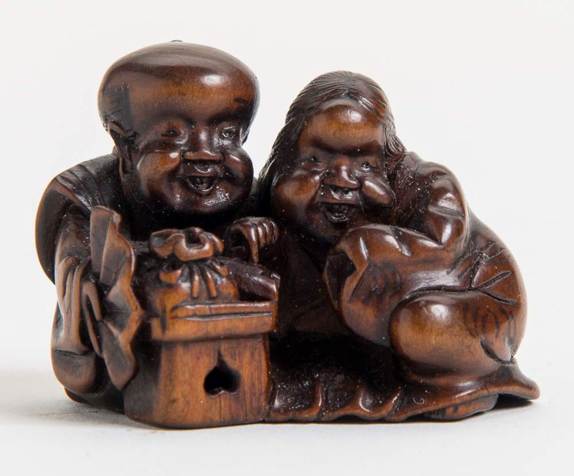 GLÜCKSZWERG FUKUSUKE MIT DER OKAME
Netsuke, Holz. Japan, 19. Jh.Sehr gut gearbeitetes Netsuke, das