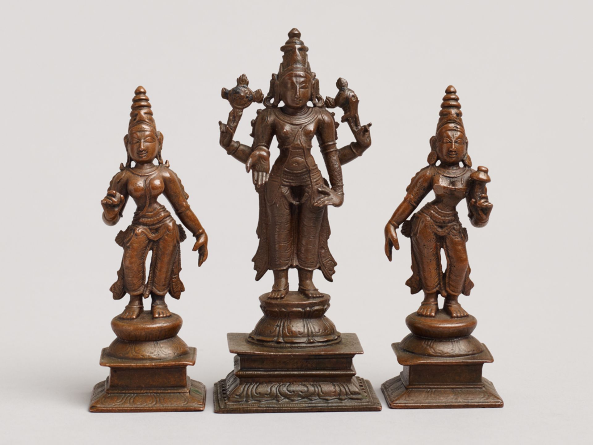 HOCHGOTTHEIT VISHNU MIT SEINEN GATTINNEN
Drei Bronzen. Indien, 19. Jh.Die mittlere größere Bronze