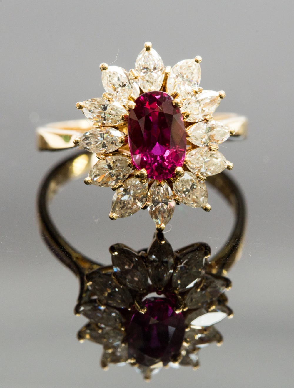 An 18ct gold, ruby and diamond cluster ring, set with an oval-cut ruby approx 1.60ct, surrounded