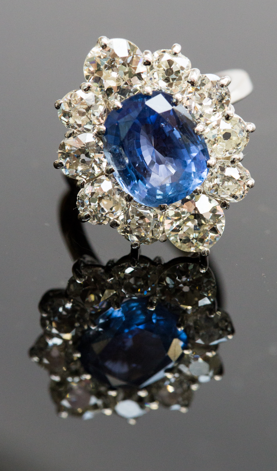 An 18ct white gold, sapphire and diamond cluster ring, the central oval-cut sapphire approx 4.