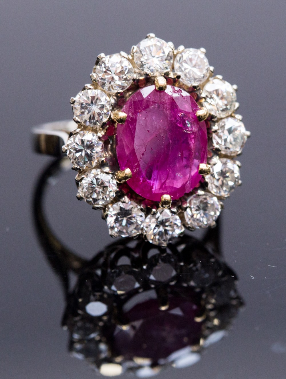 An 18ct gold, ruby and diamond cluster ring, set with an oval cut ruby, surrounded by twelve round