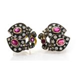 A pair of ruby and diamond earrings, each with two overlapping hearts topped with a bow, collet set